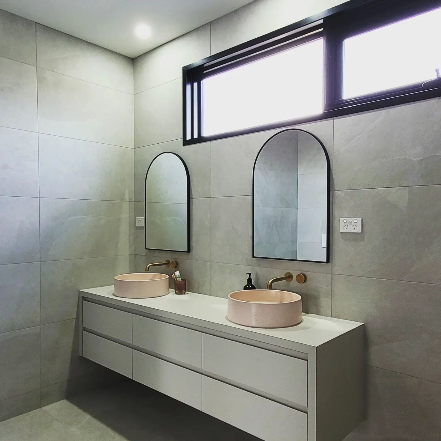 Modern double vanity bathroom with two sinks, two arched mirrors, and professional lighting installed by a new build electrician in geelong.
