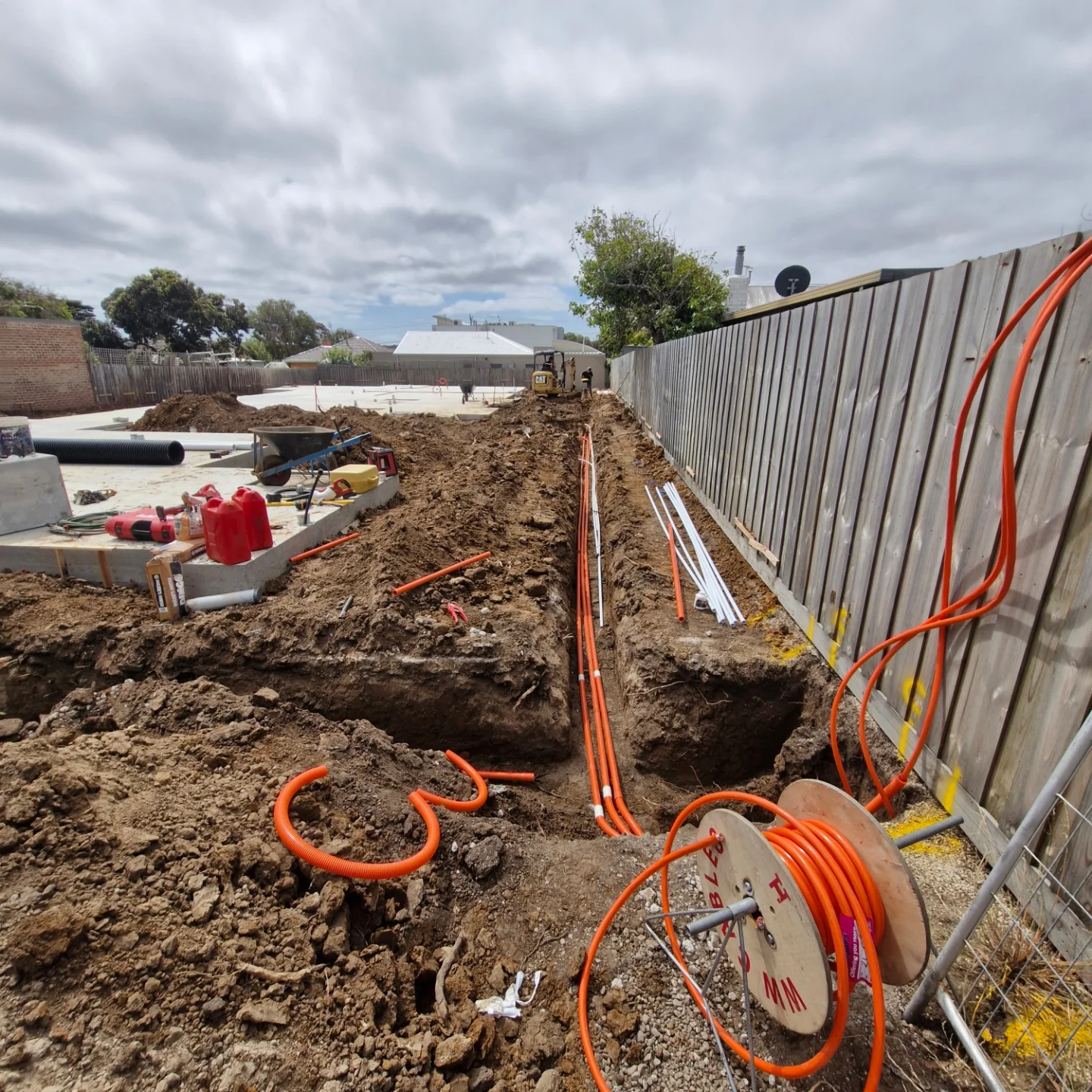 Trenching and orange electrical conduit installation along a fence line by a commercial electrician geelong